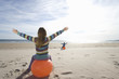 Girl and boy (8-12) on inflatable hoppers on beach, arms outstretched, rear view