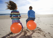Girl and boy (8-12) playing on inflatable hoppers on beach, rear view
