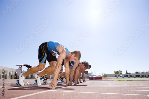 Photo: Male sprinters on starting blocks, low angle view (sun flare) Male sprinters on starting blocks, low angle view (sun flare)