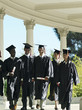 Photo: University students in graduation gowns and mortar boards walking in colonnade, smiling University students in graduation gowns and mortar boards walking in colonnade, smiling