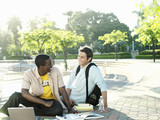 Photo: Two male university students sitting on ground with textbooks and laptop, smiling Two male university students sitting on ground with textbooks and laptop, smiling