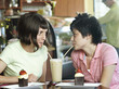 Photo: Two young women sitting at cafe table, sharing milkshake, drinking through straws, face to face Two young women sitting at cafe table, sharing milkshake, drinking through straws, face to face