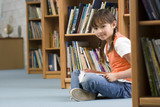 Photo: Girl (10-12) sitting on floor beside bookshelf in library, reading book, smiling, side view, portrait Girl (10-12) sitting on floor beside bookshelf in library, reading book, smiling, side view, portrait