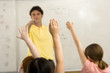 Photo: Male teacher standing beside whiteboard in classroom, children (9-11) with hands raised Male teacher standing beside whiteboard in classroom, children (9-11) with hands raised