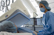 Photo: Doctor in scrubs and surgical masks scanning patient lying on hospital operating table Doctor in scrubs and surgical masks scanning patient lying on hospital operating table