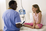 Photo: Surgeon in scrubs talking to girl (9-11) sitting in hospital bed, smiling, side view Surgeon in scrubs talking to girl (9-11) sitting in hospital bed, smiling, side view