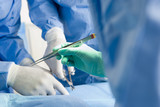 Photo: Surgeons in scrubs and surgical gloves operating on patient, focus on tweezers, close-up Surgeons in scrubs and surgical gloves operating on patient, focus on tweezers, close-up