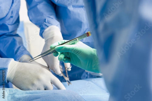 Surgeons in scrubs and surgical gloves operating on patient, focus on tweezers, close-up