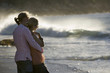Affectionate teenage couple (17-19) standing on beach near surf, boy embracing girl, side view