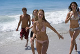 Photo: Group of teenagers (17-19) in swimwear walking on beach near water's edge, smiling, portrait Group of teenagers (17-19) in swimwear walking on beach near water's edge, smiling, portrait