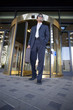 Photo: Businessman standing in front of revolving door, carrying briefcase, low angle view Businessman standing in front of revolving door, carrying briefcase, low angle view