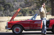 Photo: Man standing at roadside beside red convertible car with engine trouble, using mobile phone Man standing at roadside beside red convertible car with engine trouble, using mobile phone