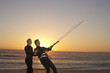 Young couple in wetsuits standing on beach at sunset, kiteboarding, side view