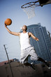 Foto: Young African American man jumping with a basketball on an urban basketball court Young African American man jumping with a basketball on an urban basketball court
