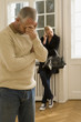 Photo: Mid adult man suffering from a headache with a young woman standing in the background Mid adult man suffering from a headache with a young woman standing in the background