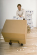 Photo: Businessman moving large cardboard box with hand truck in sparse office, packing foam on floor Businessman moving large cardboard box with hand truck in sparse office, packing foam on floor