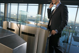 Photo: Businessman placing card in security barrier, using mobile phone, smiling, side view (tilt) Businessman placing card in security barrier, using mobile phone, smiling, side view (tilt)