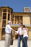 Photo: Young couple shaking hands with architect in front of partially built house, low angle view Young couple shaking hands with architect in front of partially built house, low angle view