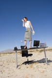 Photo: Businesswoman standing on desk in desert, shouting into telephone receiver, low angle view Businesswoman standing on desk in desert, shouting into telephone receiver, low angle view