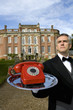 Mature butler with telephone on tray by manor house, low angle view