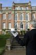 Mature butler with tray of tea by manor house, rear view