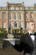 Mature butler with drinks on tray by manor house, close-up