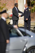 Photo: Businessman and colleague shaking hands by chauffeur holding door of car open (differential focus) Businessman and colleague shaking hands by chauffeur holding door of car open (differential focus)