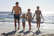 Photo: Two generation family wearing swimwear, walking away from surf on sandy beach, side by side, holding hands, front view, smiling Two generation family wearing swimwear, walking away from surf on sandy beach, side by side, holding hands, front view, smiling