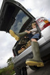 Boy (8-10) putting on wellington boots, sitting in boot of stationary car, smiling, portrait, low angle view (tilt)