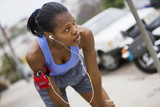 Photo: Exhausted female jogger stopping for breath on pavement, leaning on knees, listening to MP3 player strapped to arm, focus on foreground (tilt) Exhausted female jogger stopping for breath on pavement, leaning on knees, listening to MP3 player strapped to arm, focus on foreground (tilt)