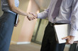 Photo: Businessman and businesswoman shaking hands in office corridor, side view, mid-section (tilt) Businessman and businesswoman shaking hands in office corridor, side view, mid-section (tilt)