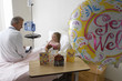 Photo: Girl (7-9) sitting in hospital bed, talking to doctor, balloon and cards in foreground, side view Girl (7-9) sitting in hospital bed, talking to doctor, balloon and cards in foreground, side view