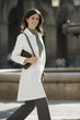 Photo: Woman in polo neck jumper and white coat walking in plaza, carrying handbag, smiling, portrait Woman in polo neck jumper and white coat walking in plaza, carrying handbag, smiling, portrait