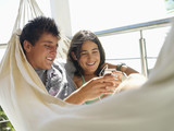 Photo: Teenage couple (15-17) relaxing in hammock on balcony, listening to MP3 player, smiling, close-up Teenage couple (15-17) relaxing in hammock on balcony, listening to MP3 player, smiling, close-up