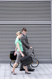 Photo: Businessman walking with businesswoman on pavement, man pushing folding commuter bicycle Businessman walking with businesswoman on pavement, man pushing folding commuter bicycle