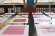 Photo: Woman looking at various designs arranged on large table in office, surface level Woman looking at various designs arranged on large table in office, surface level