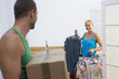Photo: Couple moving house, woman packing clothing in bedroom, man carrying sealed box, smiling Couple moving house, woman packing clothing in bedroom, man carrying sealed box, smiling