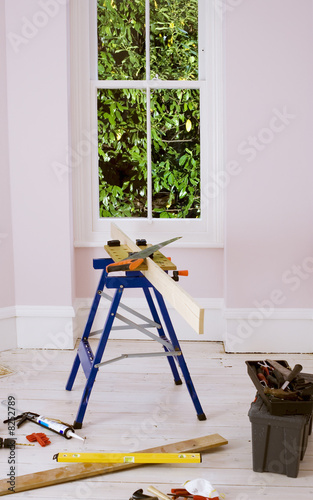 Photo: Workbench, saw, plank of wood and toolbox in room Workbench, saw, plank of wood and toolbox in room