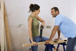 Foto: Couple doing DIY at home, woman drilling hole with power drill on workbench, man assisting, smiling Couple doing DIY at home, woman drilling hole with power drill on workbench, man assisting, smiling