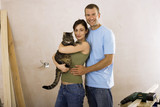 Photo: Couple doing DIY at home, woman holding domestic cat, man embracing woman, smiling, portrait Couple doing DIY at home, woman holding domestic cat, man embracing woman, smiling, portrait