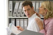 Photo: Businesswoman with hands on neck and shoulder of businessman with file by shelves, side view Businesswoman with hands on neck and shoulder of businessman with file by shelves, side view