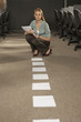 Businesswoman holding a file and crouching in an office in front of a row of papers