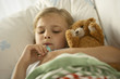 Photo: High angle view of a girl lying on the bed and measuring her temperature with a thermometer High angle view of a girl lying on the bed and measuring her temperature with a thermometer