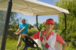 Photo: Mid adult woman sitting in a golf cart with a mid adult man playing golf in the background Mid adult woman sitting in a golf cart with a mid adult man playing golf in the background