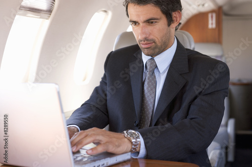 Photo: A businessman using a laptop in a plane A businessman using a laptop in a plane