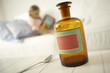 Photo: Close-up of a medicine bottle and a spoon on a table with a girl sitting on the bed in the background Close-up of a medicine bottle and a spoon on a table with a girl sitting on the bed in the background
