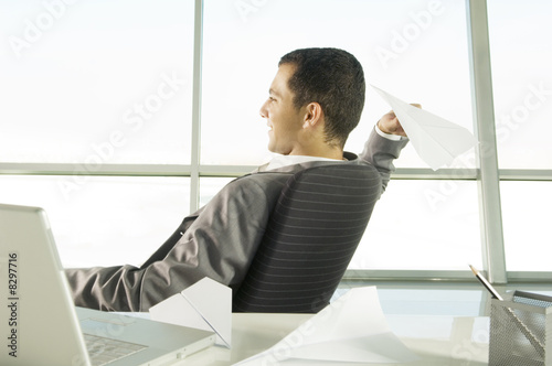 Photo: A businessman sitting at a desk making paper airplanes A businessman sitting at a desk making paper airplanes