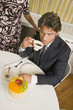 Photo: High angle view of a young man holding a cup of tea and sitting in front of a cake High angle view of a young man holding a cup of tea and sitting in front of a cake