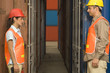 Side profile of two dock workers standing in front of cargo containers