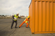 Photo: Male dock worker pushing a cargo container with a businessman standing beside him Male dock worker pushing a cargo container with a businessman standing beside him